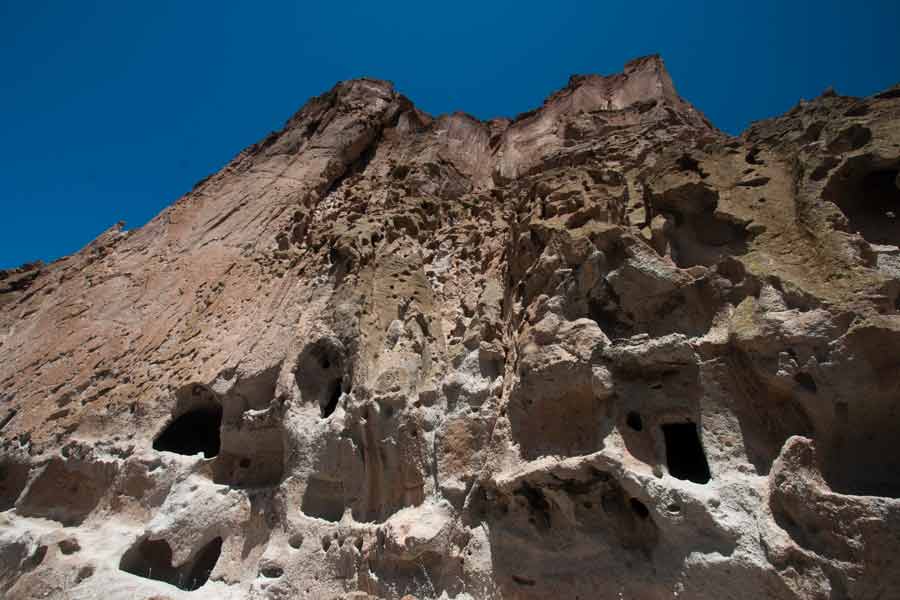 The cliff face towers above where the dwellings are.