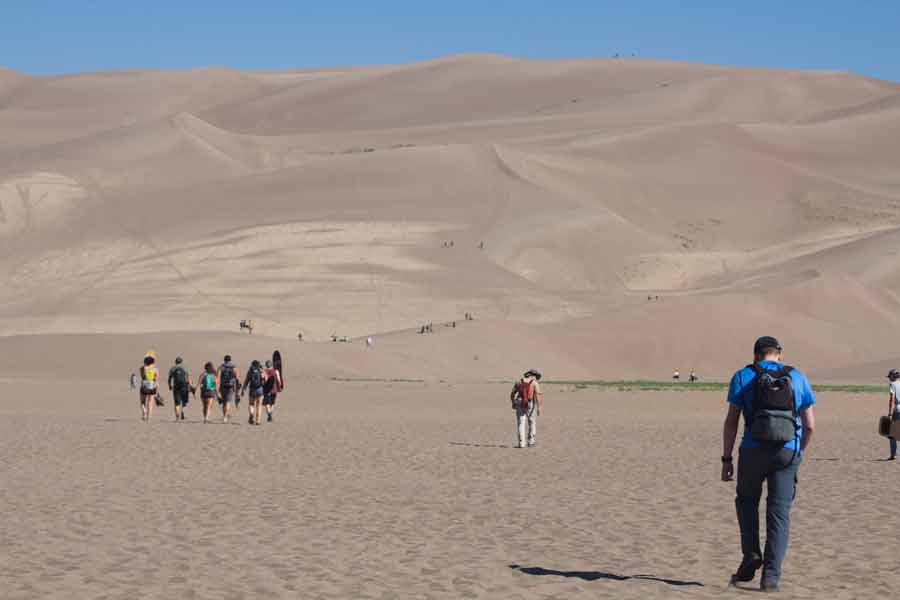 People walk toward the dune to climb it.
