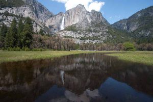 river flows through the meadow with waterfall in background in